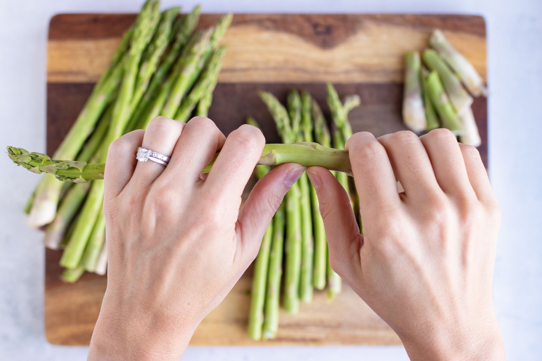 A hand breaks an asparagus spear end off.