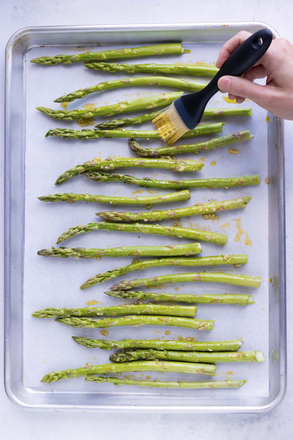 A brush rubs seasoning onto aspargus spears.