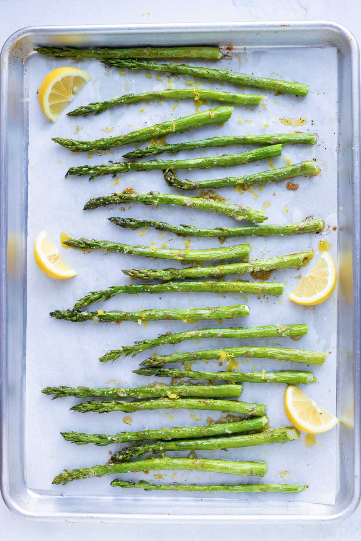 Asparagus that has been roasted in the oven on a baking sheet with lemon wedges.