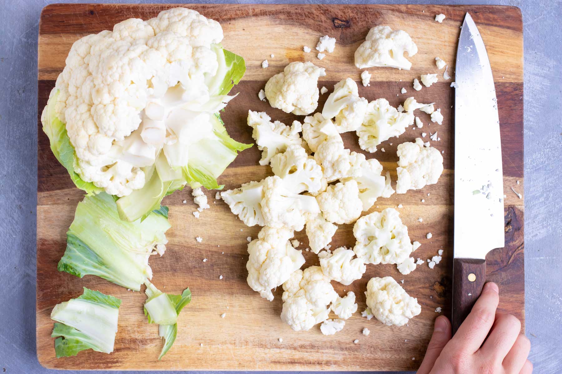 A head of cauliflower that is being cut into florets on a wooden cutting board.