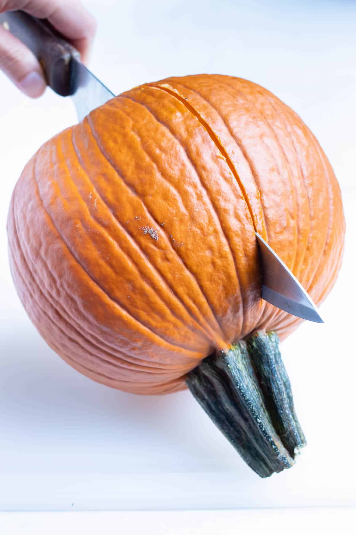 Pumpkin is cut in half with a large knife.