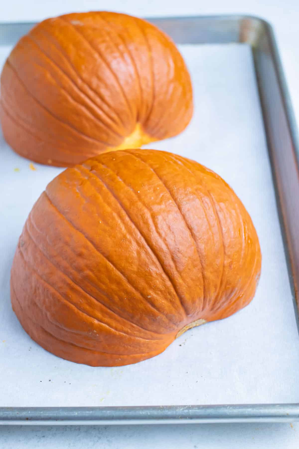 Pumpkin halves are laid hollow-side down on the baking sheet.