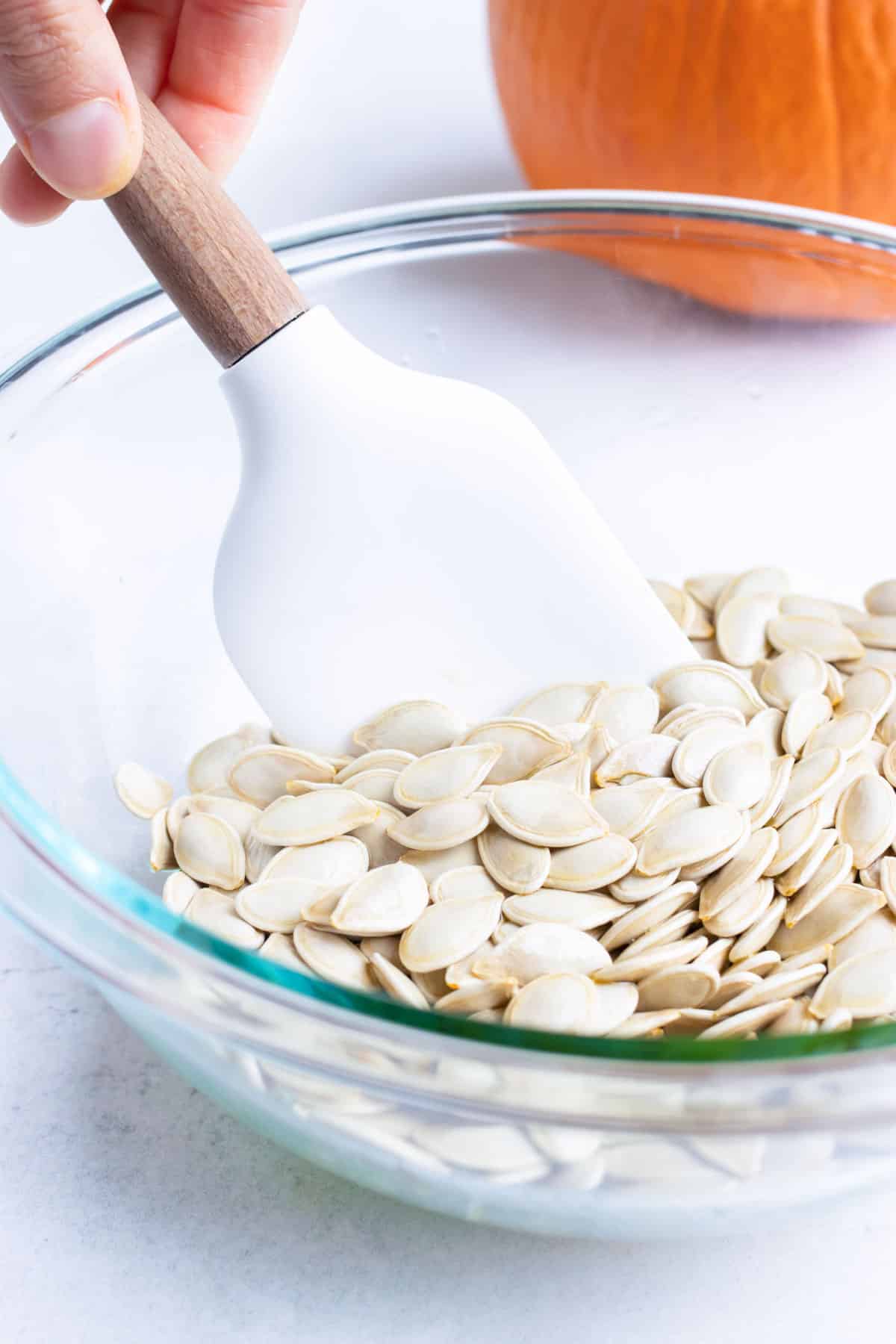 Oil or butter, pumpkin seeds, and seasonings are combined in a bowl and mixed.