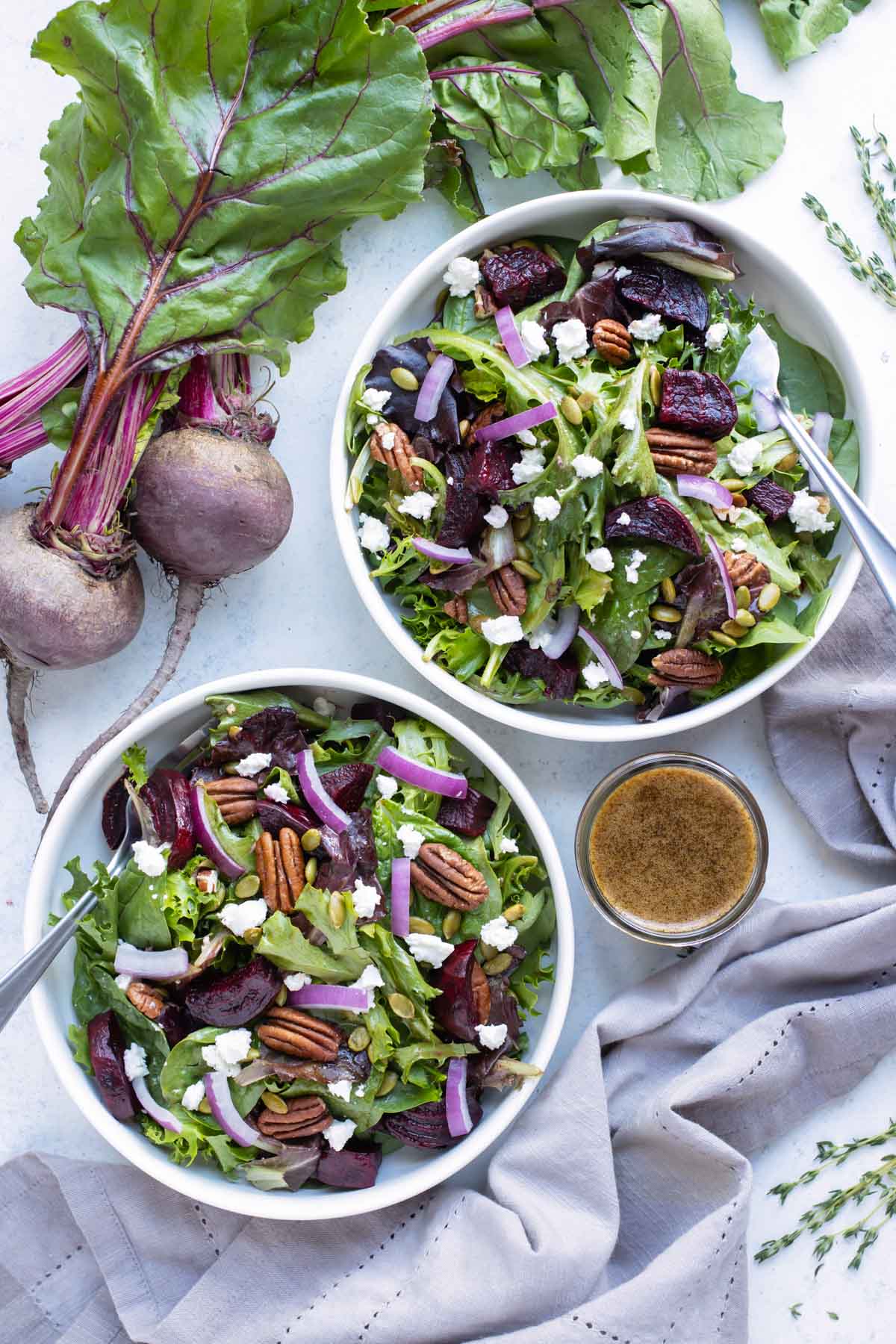 Two bowls of roasted beet salad with goat cheese are served next to a bunch of fresh beets.