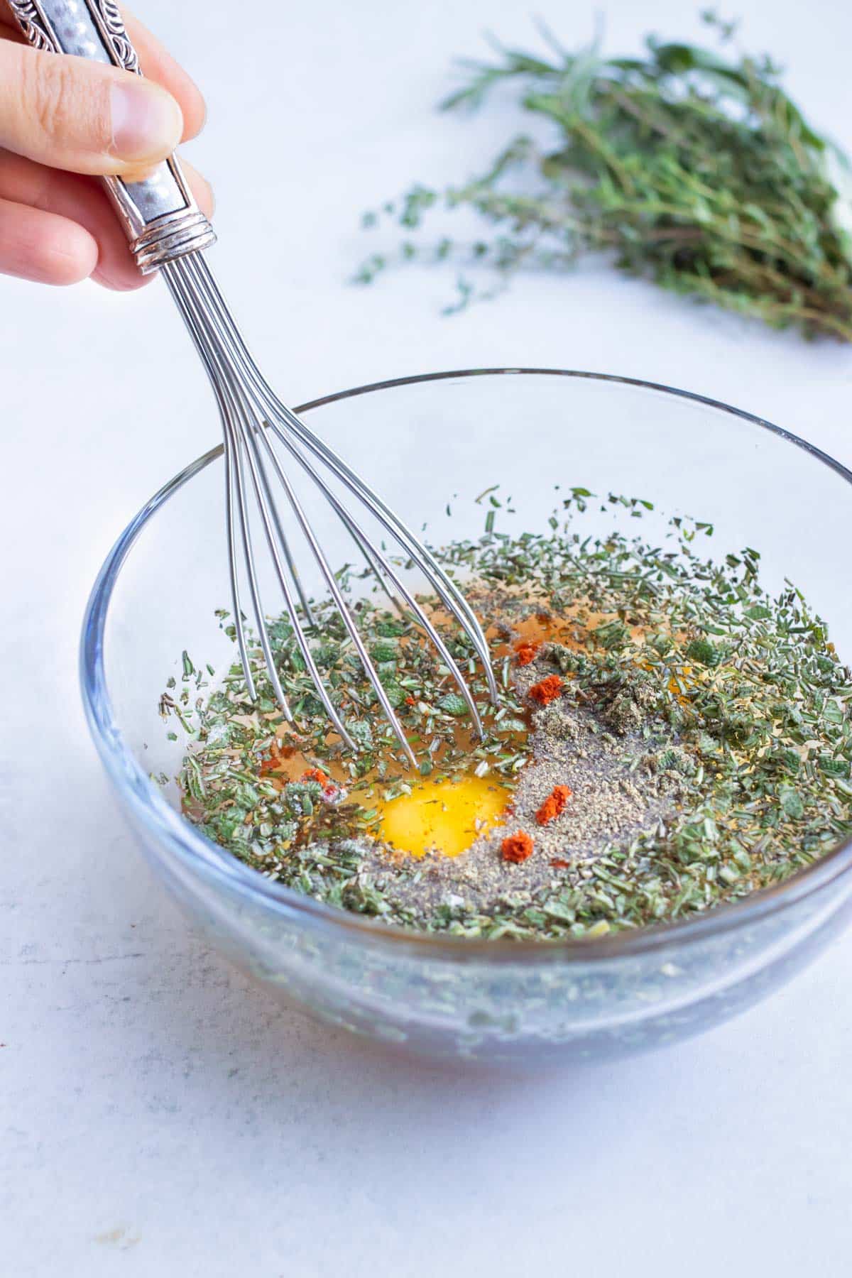 Eggs, spices, herbs, and chicken broth are whisked together in a glass bowl.