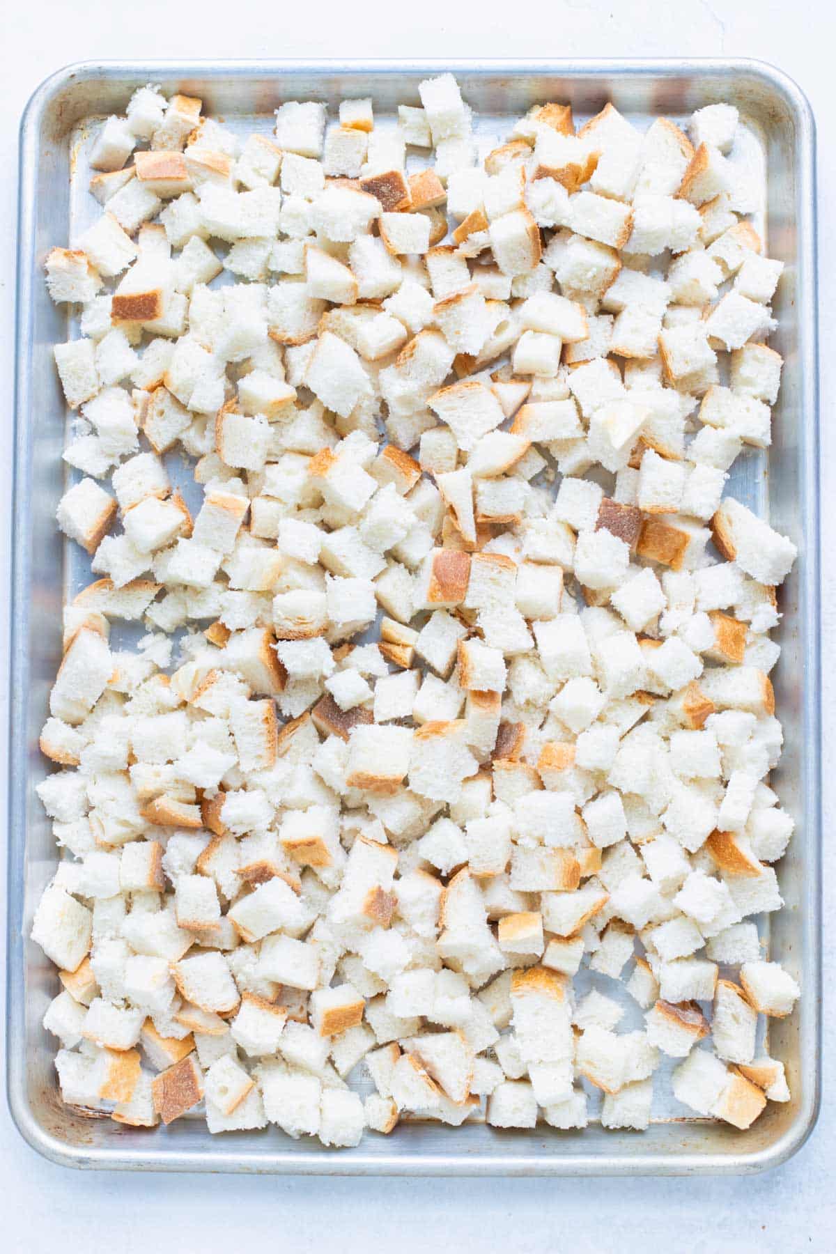 Bread cubes are placed on a baking sheet and toasted in the oven.