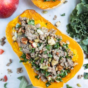 A sausage, kale, and apple mixture are used to fill a roasted butternut squash.