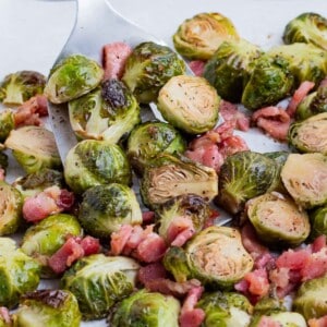 A spatula is used to scoop Brussels sprouts and bacon after roasting in the oven.