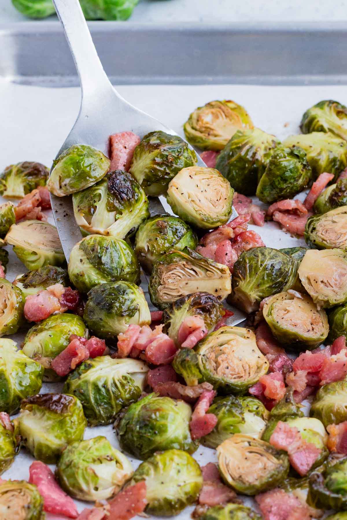 A spatula is used to scoop Brussels sprouts and bacon after roasting in the oven.
