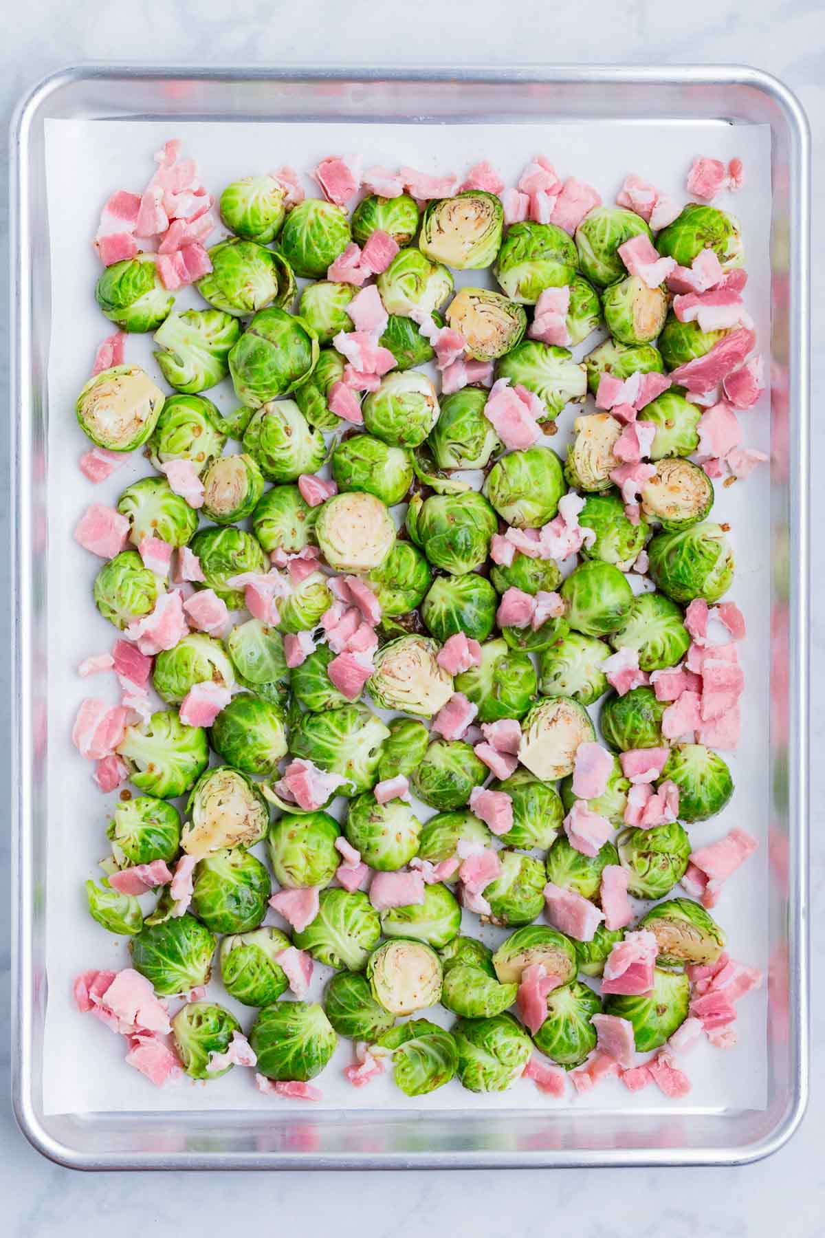Coated Brussels sprouts and bacon are arranged on a baking sheet.
