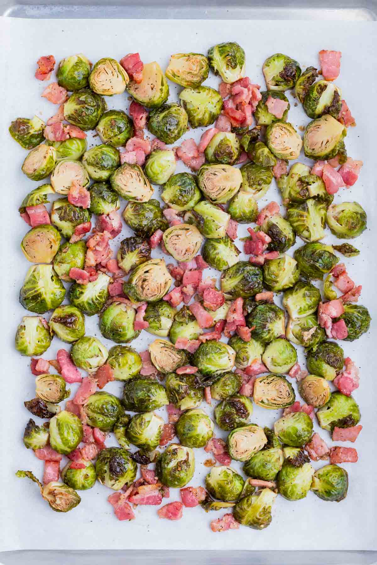 Brussels sprouts and bacon cook together on a baking sheet in the oven.