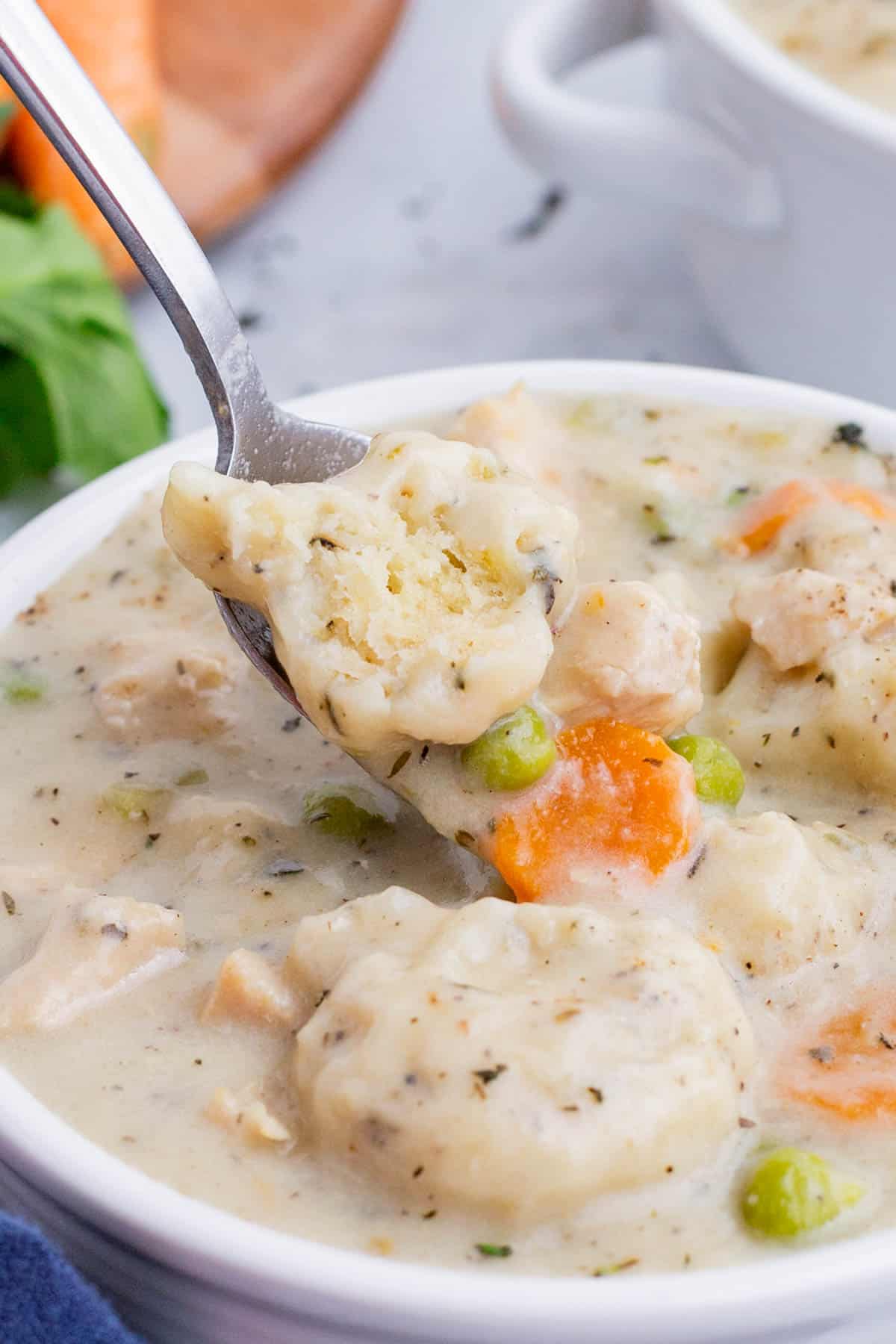 A spoon scoops out a serving of chicken dumpling soup with carrots and celery.