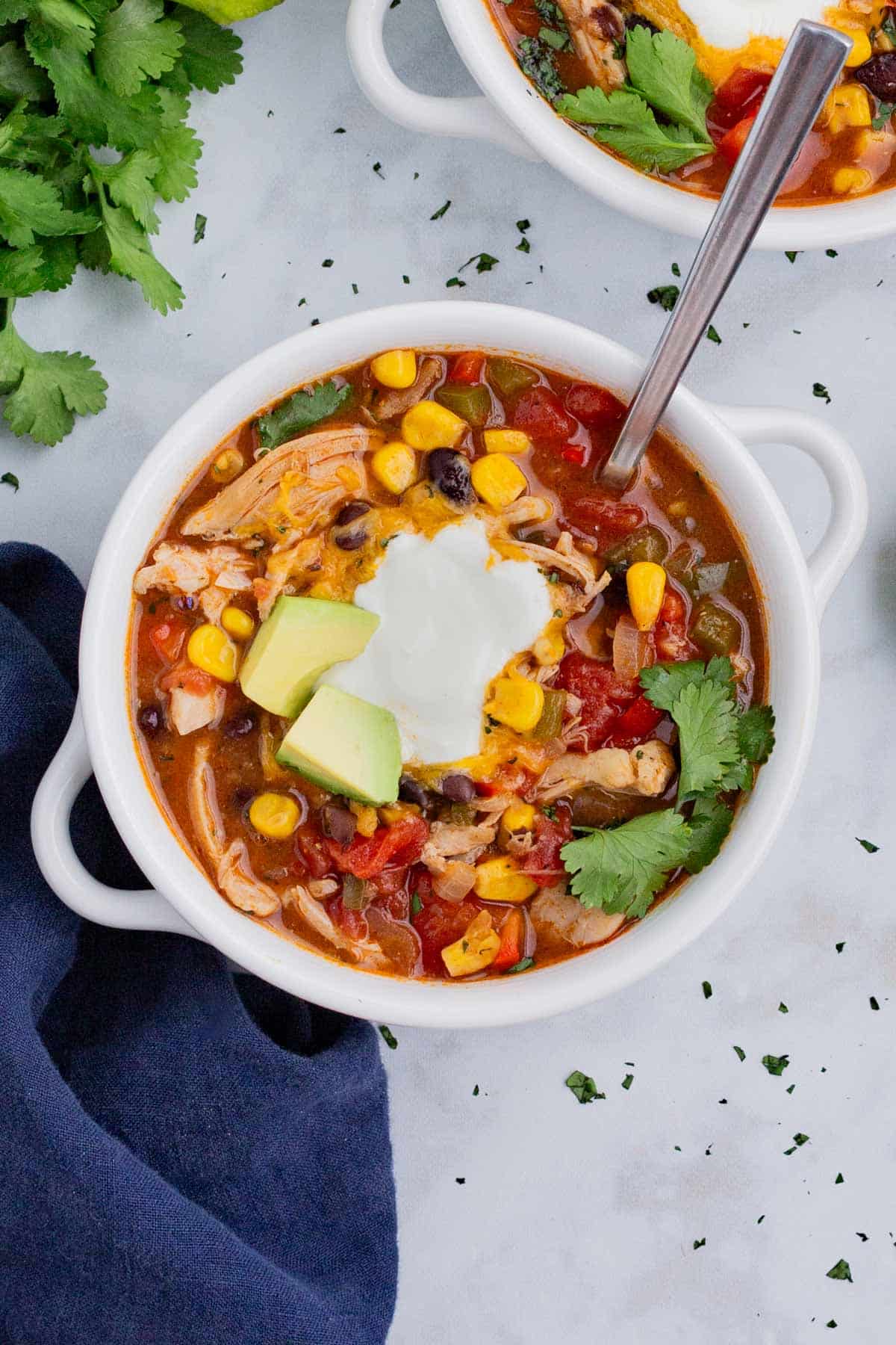An overhead shot of chicken enchilada soup in a white bowl topped with cheese and sour cream.