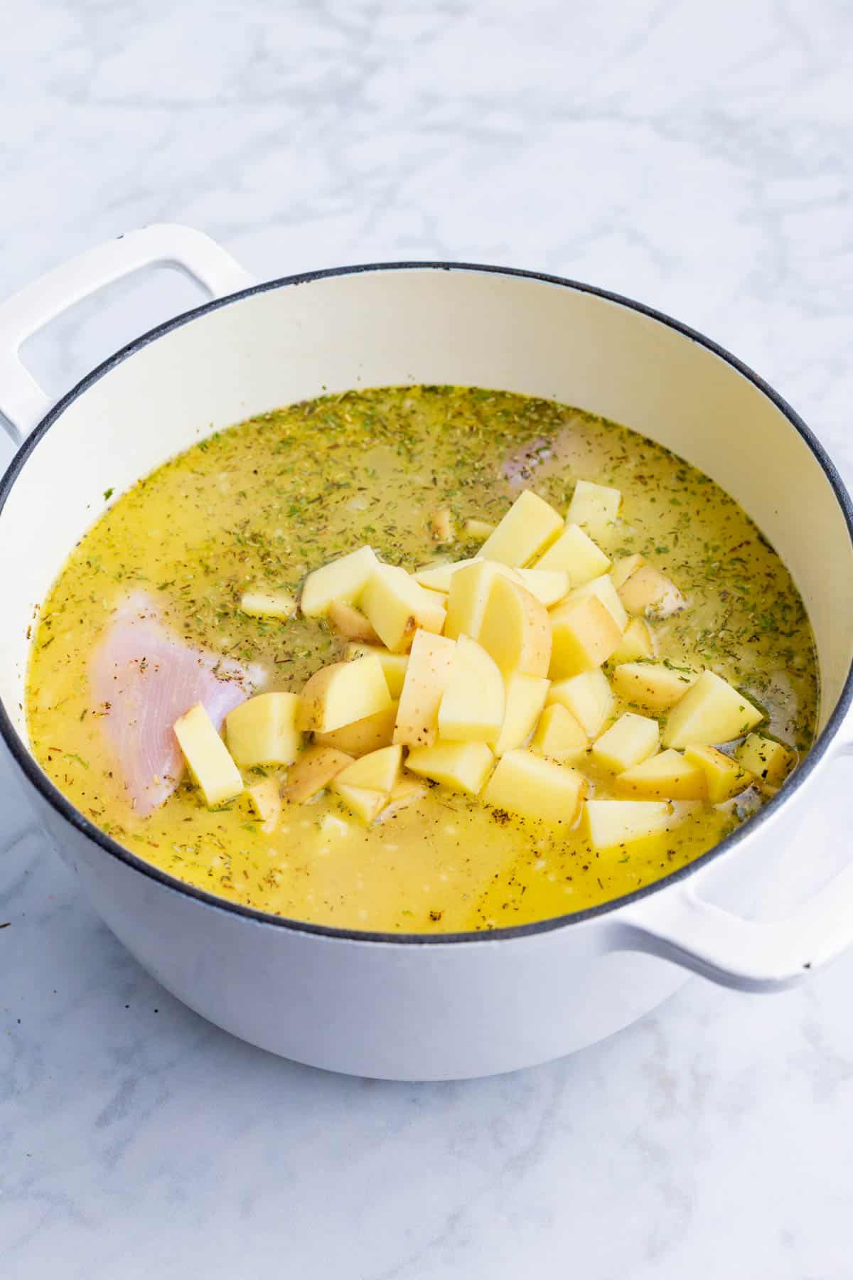 Potatoes, chicken, and herbs are added to the broth mixture.