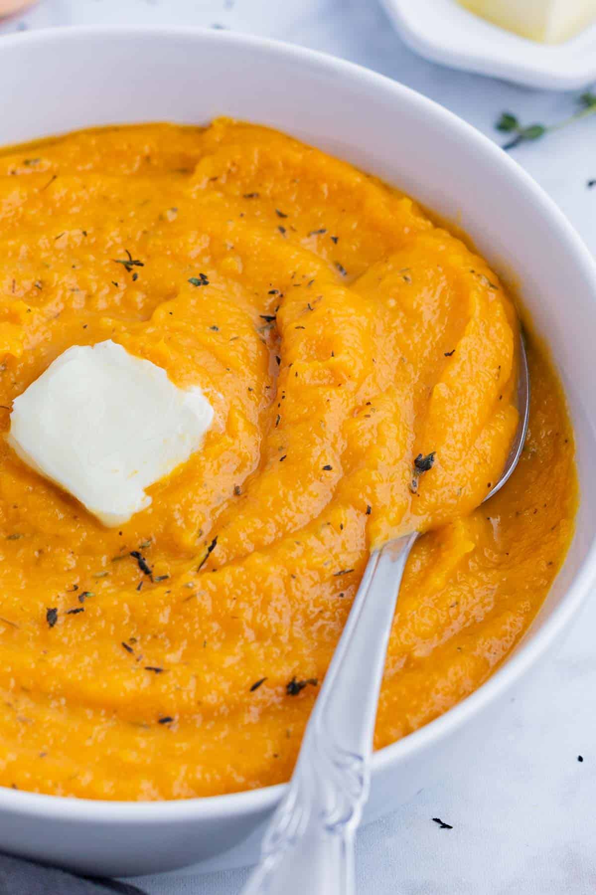 An overhead view of mashed butternut squash in a white bowl with a spoon.