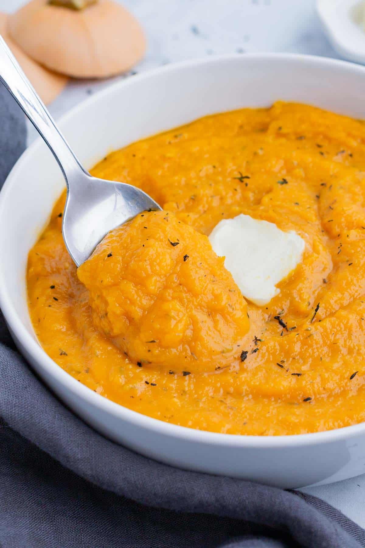Mashed Butternut Squash RECIPE served in a white bowl and a spoon garnished with butter.