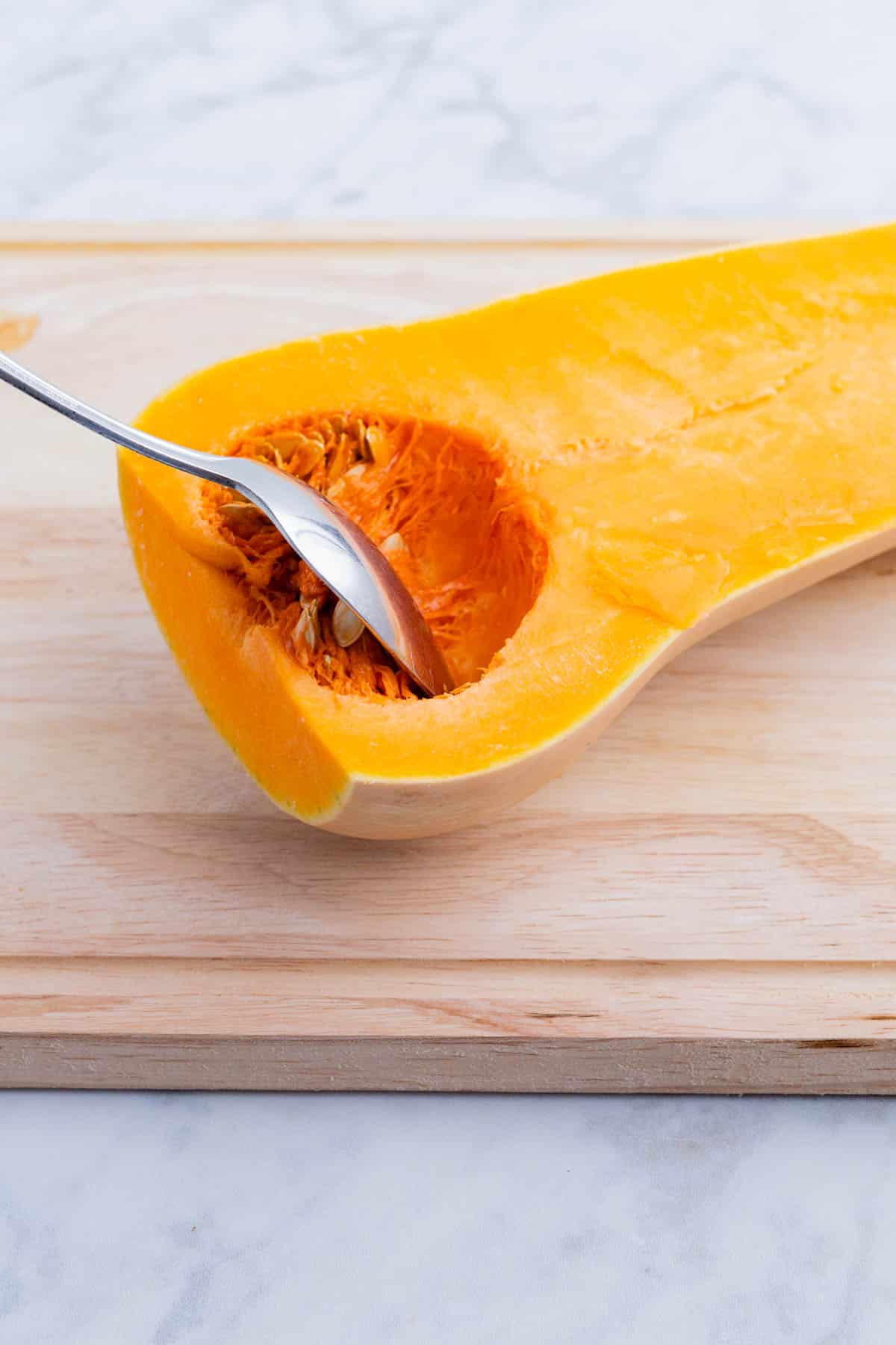 A spoon removes the insides of the butternut squash.