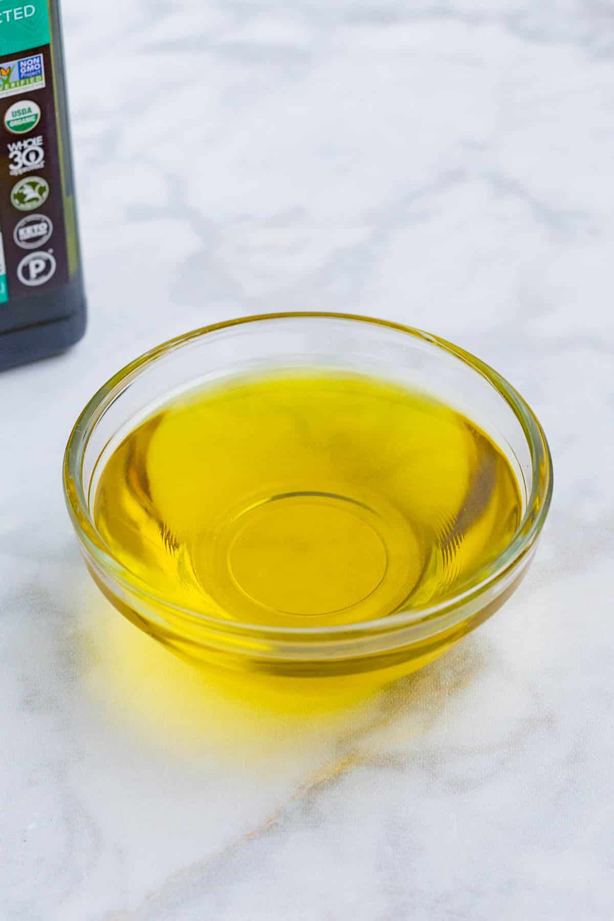 Olive oil in a small glass bowl with its original container in the background.