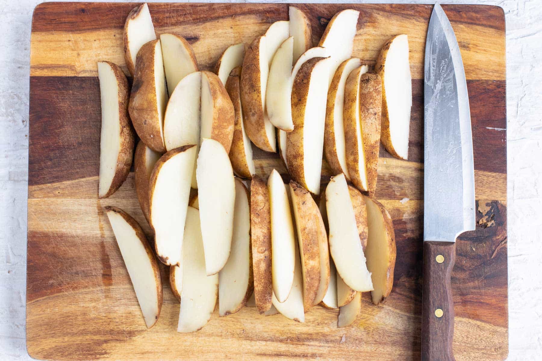 Potatoes are sliced into wedges on a cutting board.