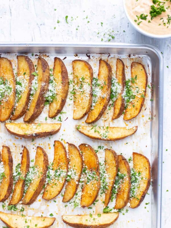 A large baking sheet full of a baked potato wedges recipe with Parmesan cheese and parsley on top.