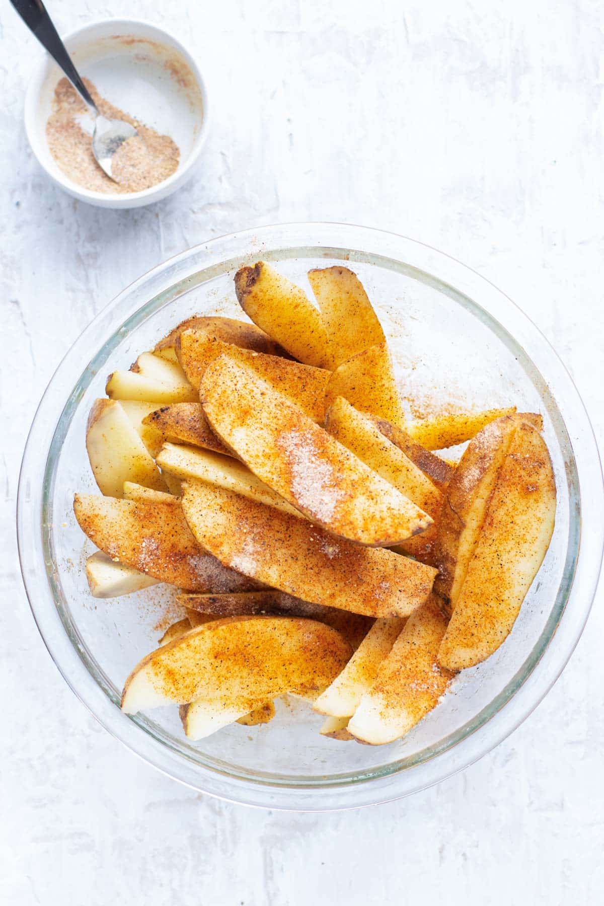 A bowl of Russet potatoes that have been cut into wedges and are being tossed with a seasoning blend.