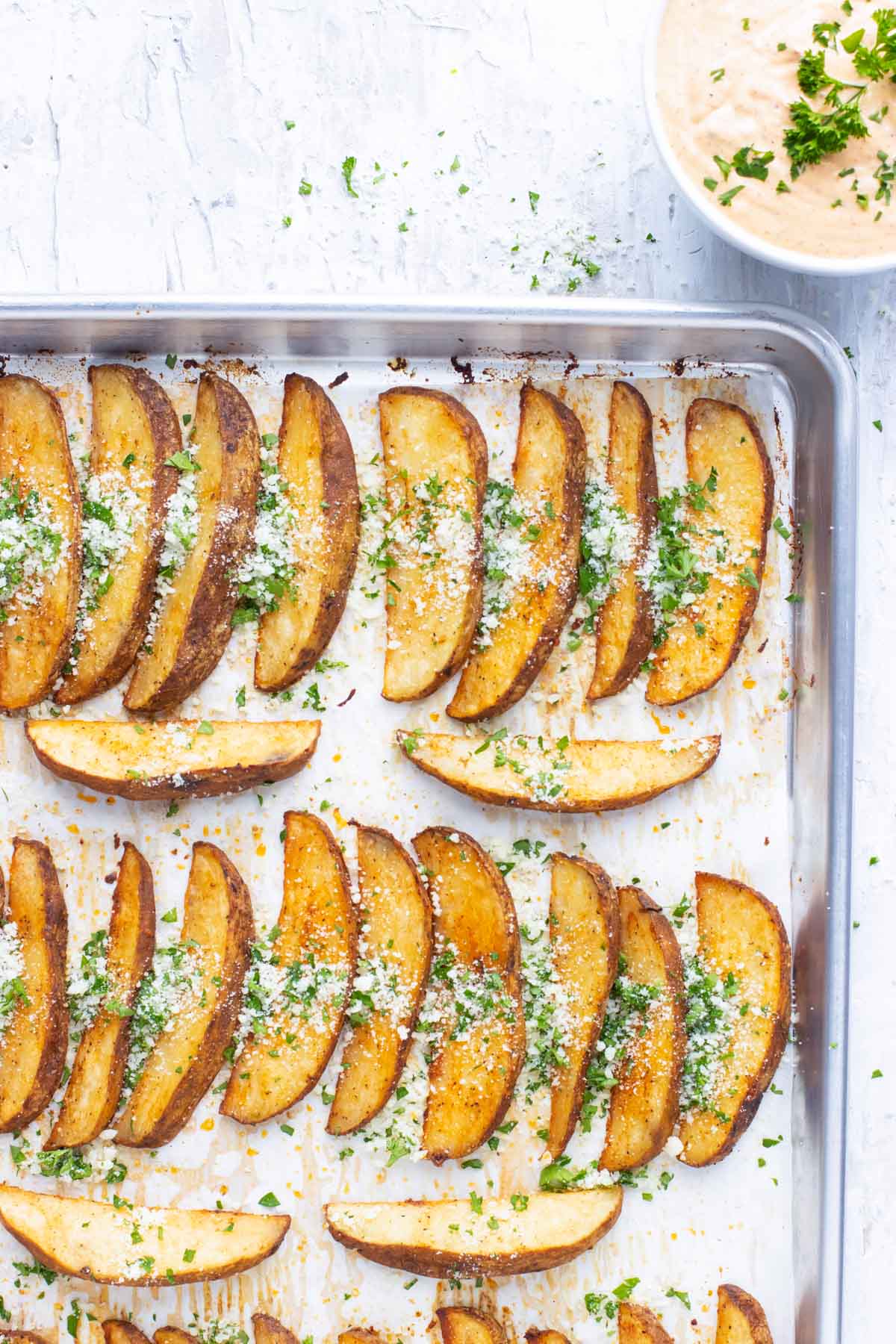 Crispy Baked Potato Wedges RECIPE on a sheet pan with garnishes.