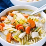 A bowl filled with gluten-free chicken soup with a spoon inside.