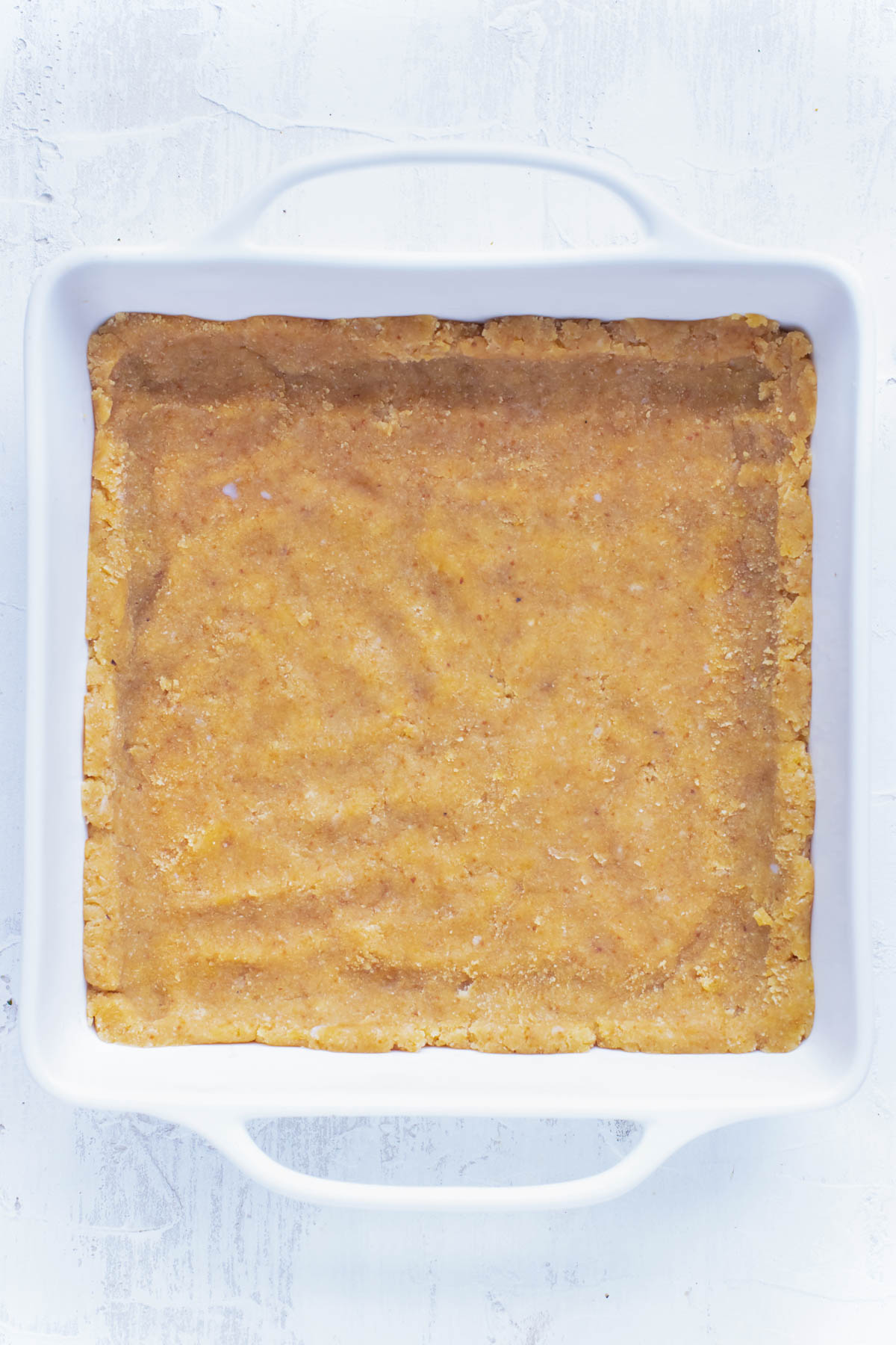 A shortbread crust is pressed into a baking dish.