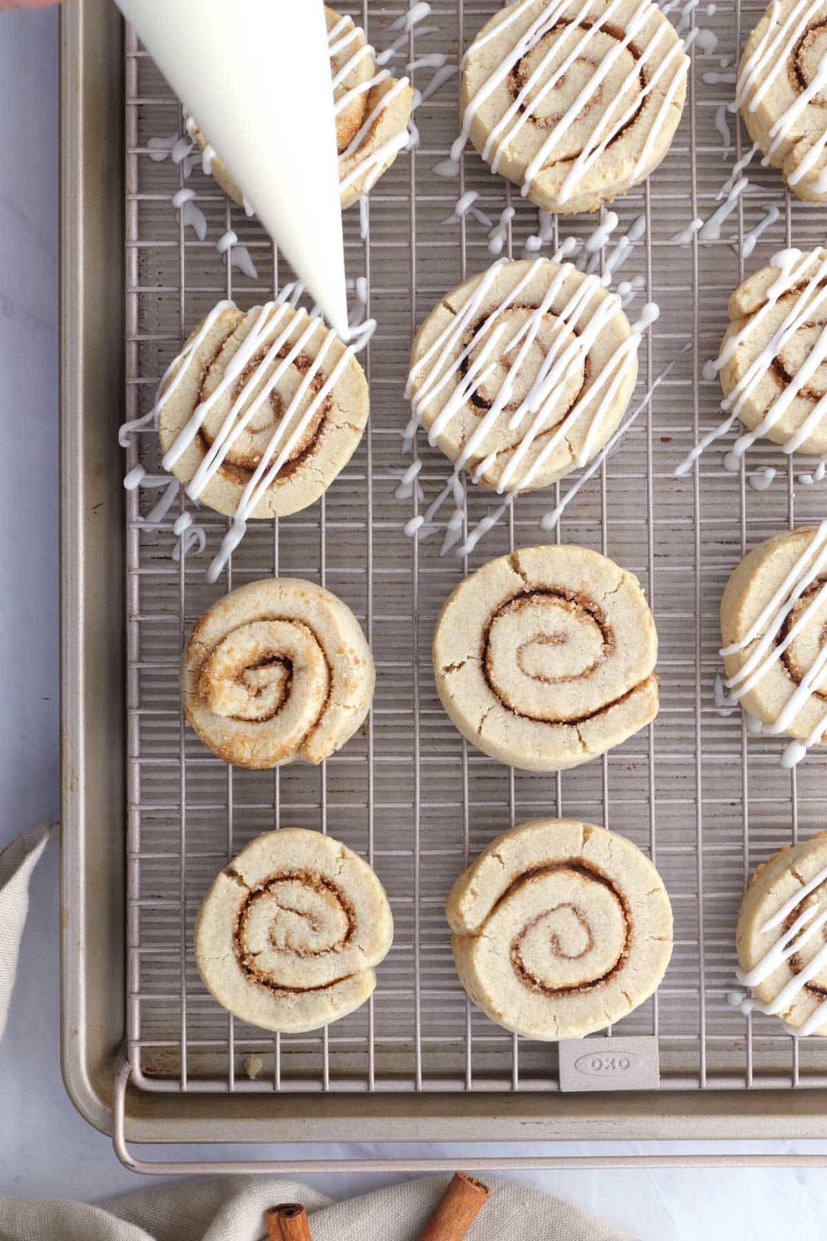 Cinnamon roll cookies are iced on a wire rack.