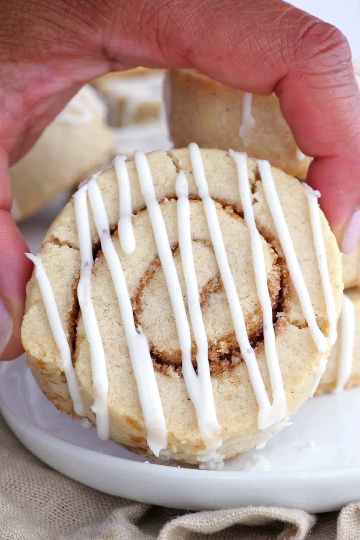 A hand holds an iced cinnamon roll cookie.