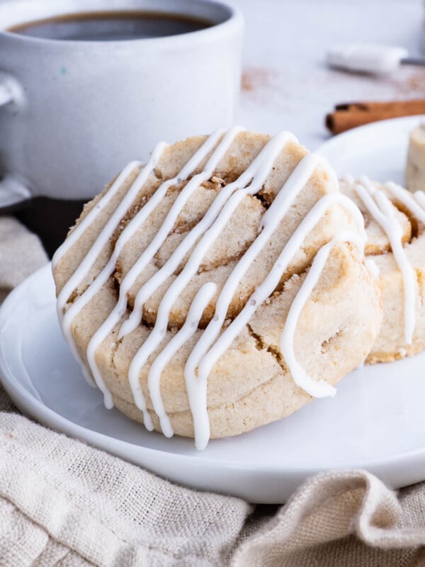 Two cinnamon Roll cookies are served on a white plate with coffee.