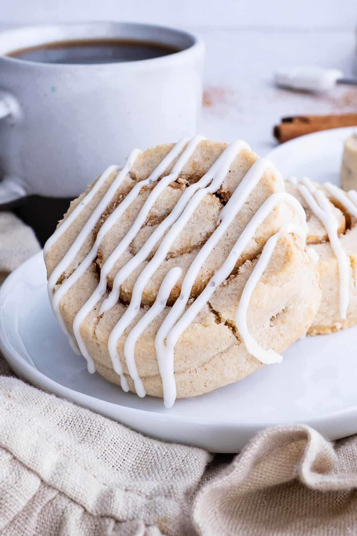 Two cinnamon Roll cookies are served on a white plate with coffee.