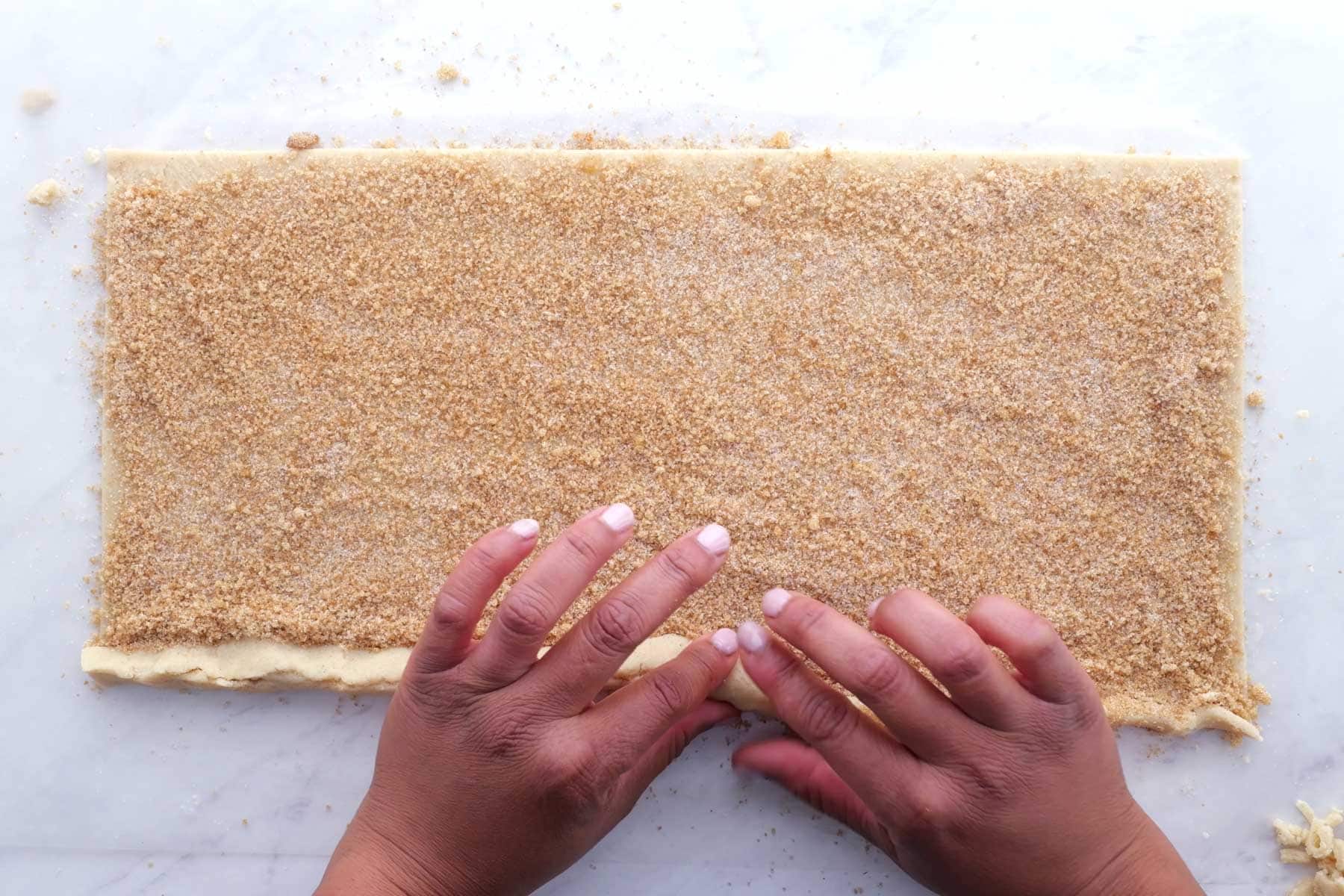 Rolled out dough is topped with cinnamon sugar and rolled from the edge.