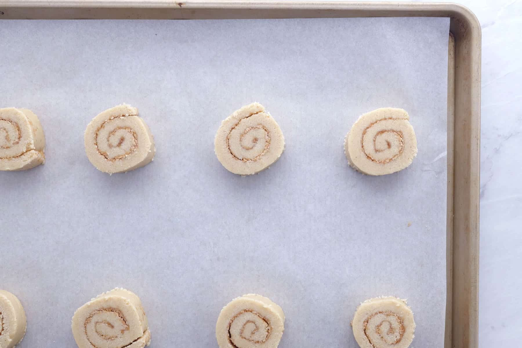 Cinnamon roll cookies are spaced out on a baking sheet.