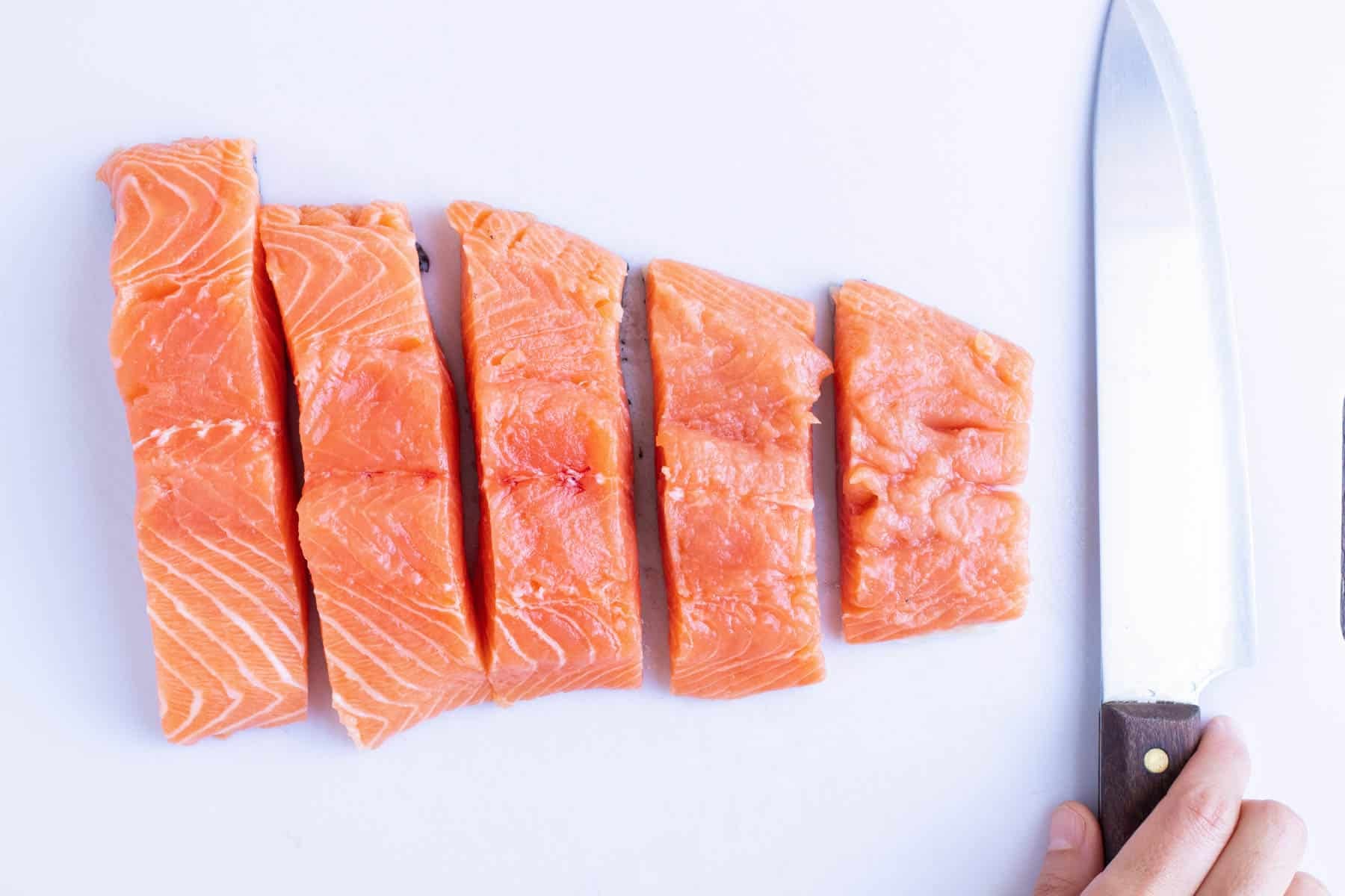 A salmon fillet cut into five even pieces on a white cutting board for easy salmon curry.