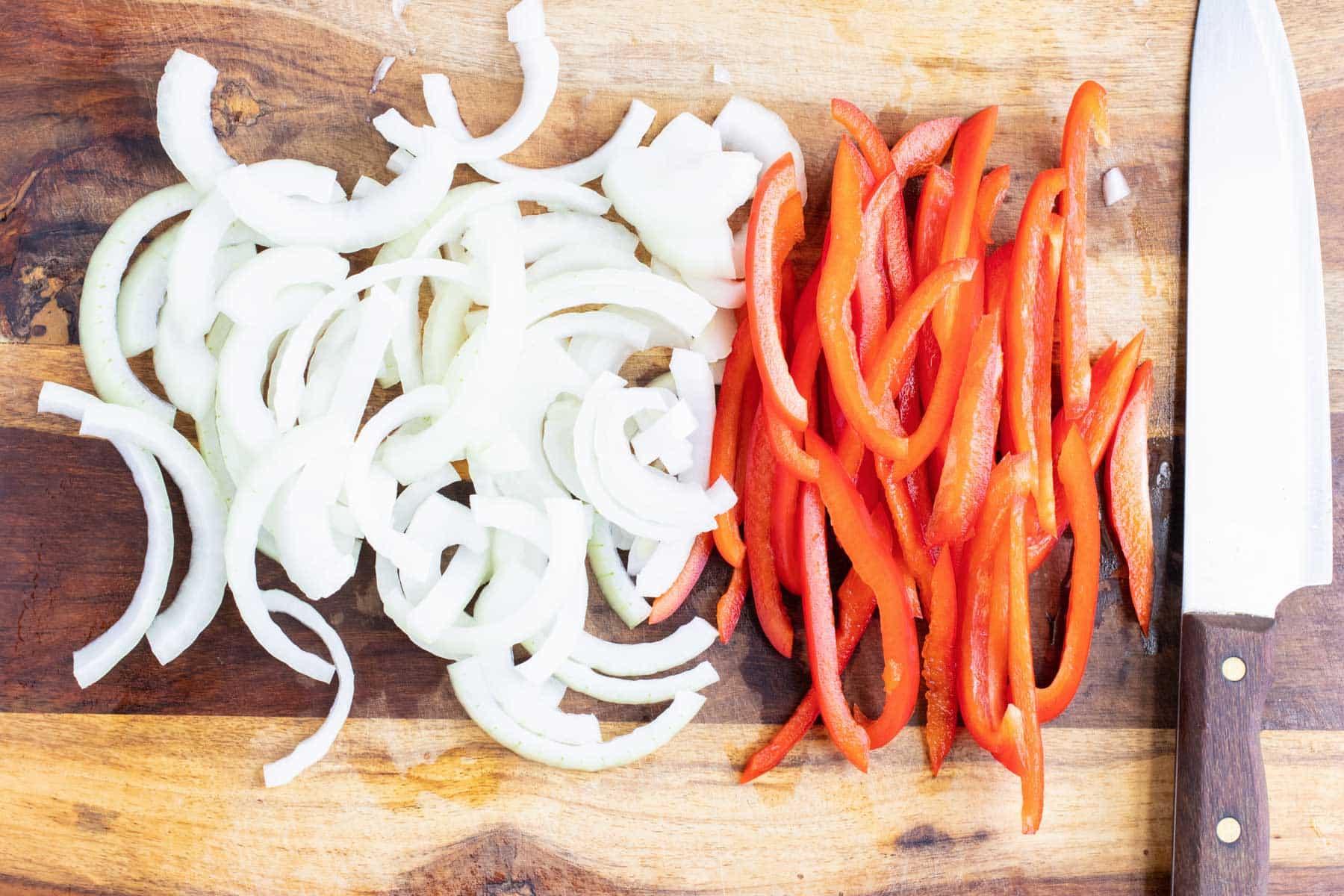 Thinly sliced sweet onion and red bell pepper on a cutting board for one-pan salmon curry.
