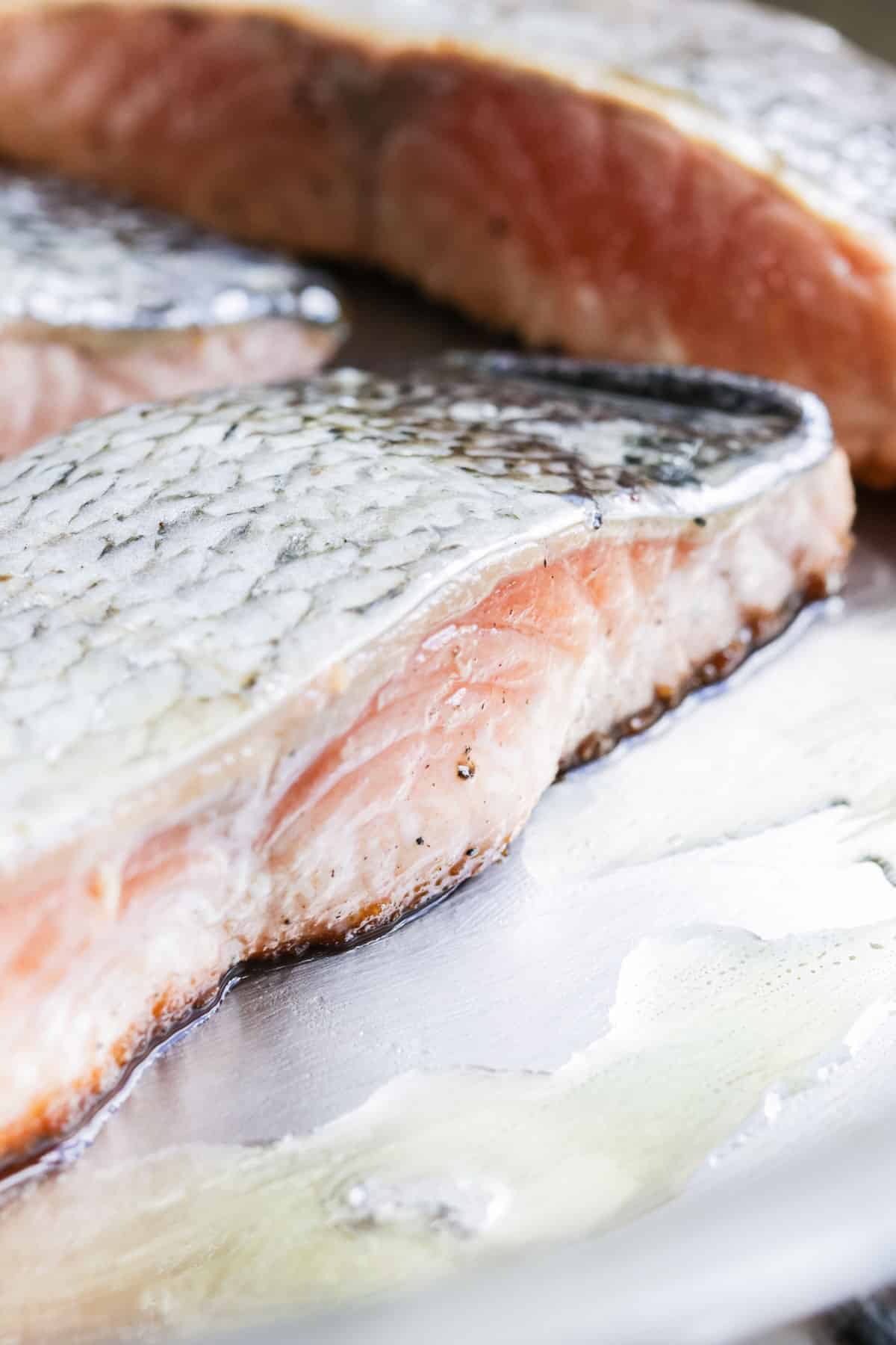 A raw salmon filet being seared in a stainless steel skillet.