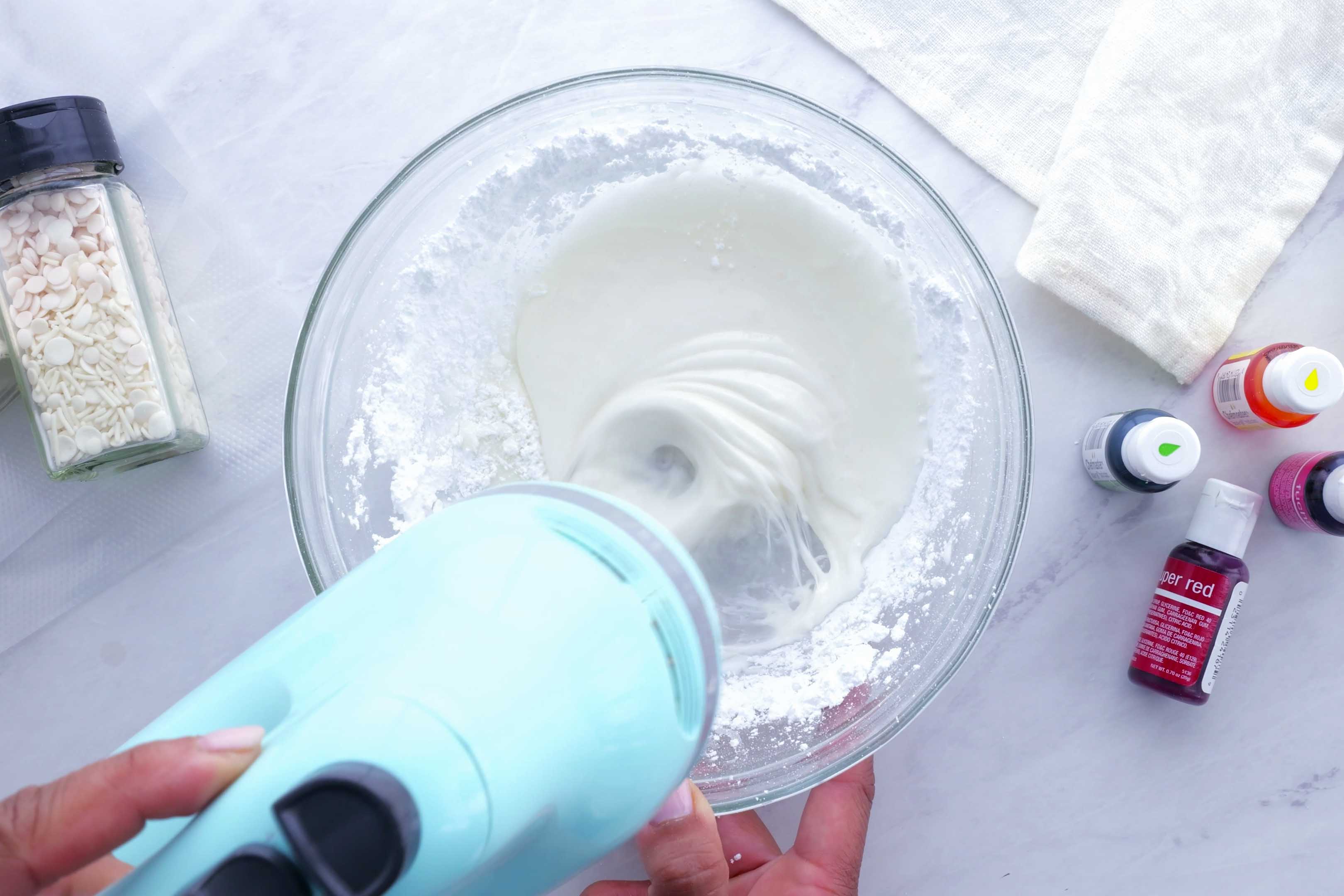 A handheld mixture stirs the icing ingredients.
