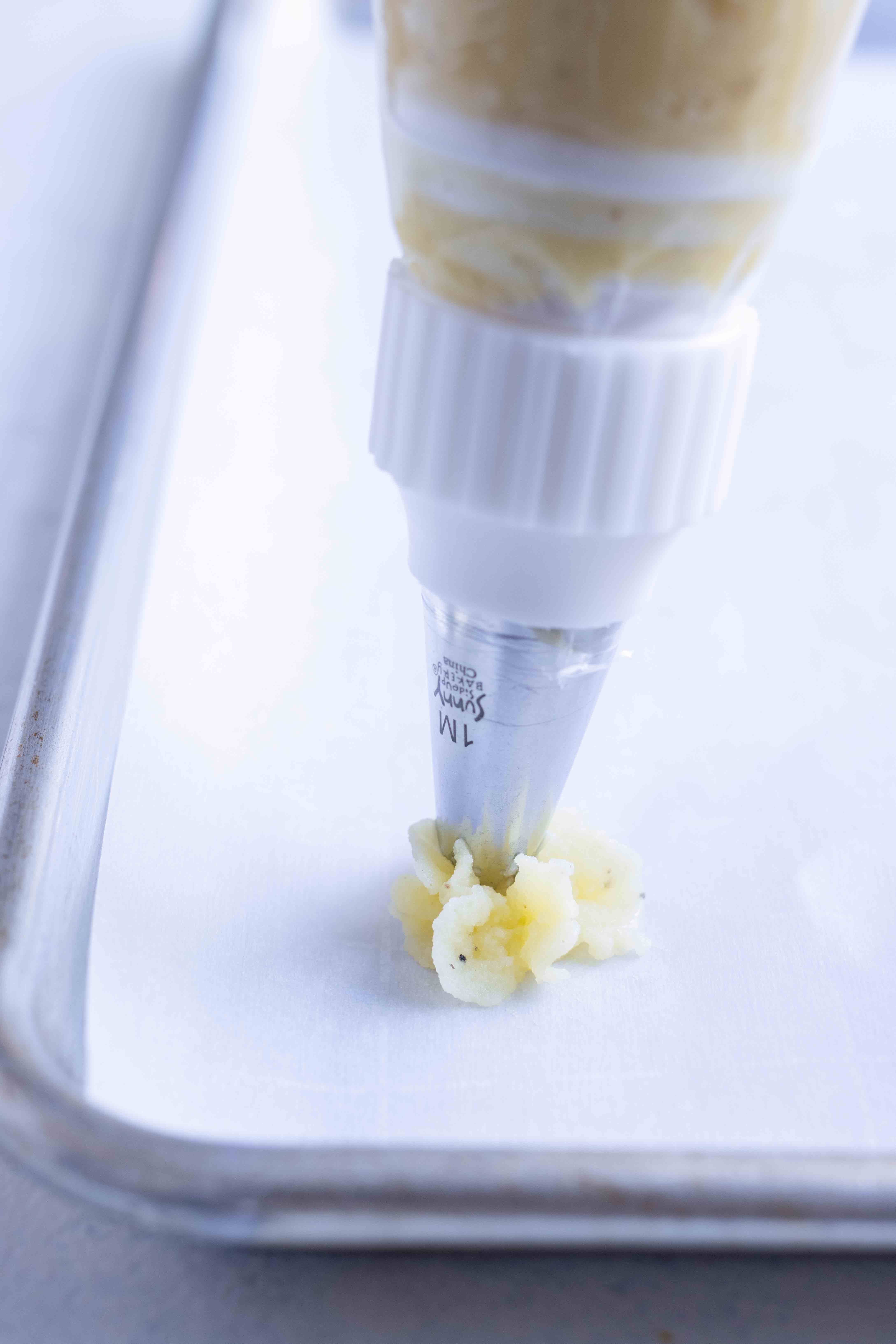 Piping make-ahead duchess potatoes onto a parchment lined baking sheet