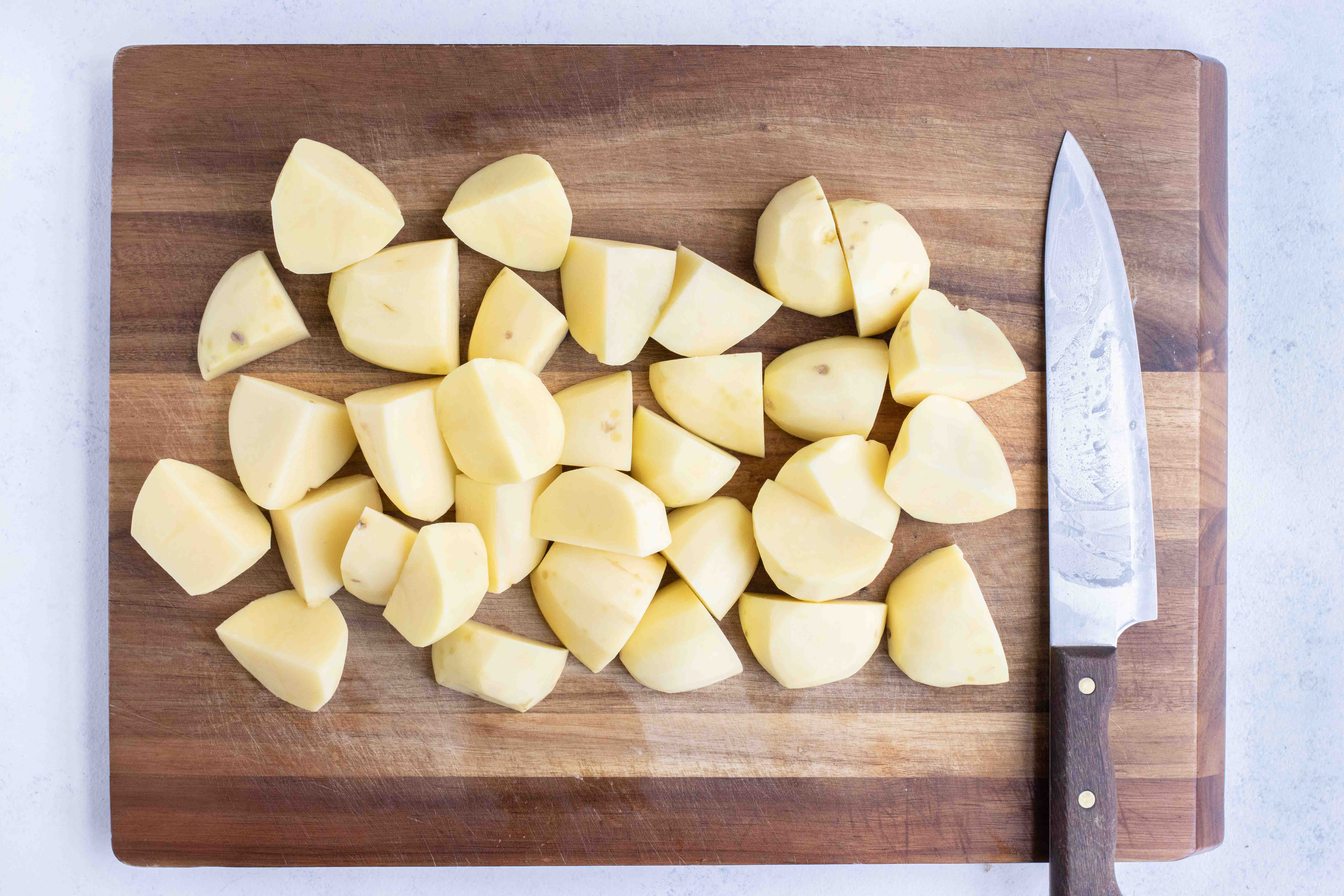 Cubed potatoes are set on the cutting board by a knife.