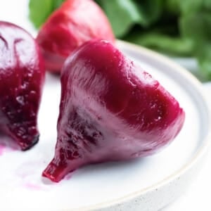 Boiled beets that have been peeled are sitting on a white plate.