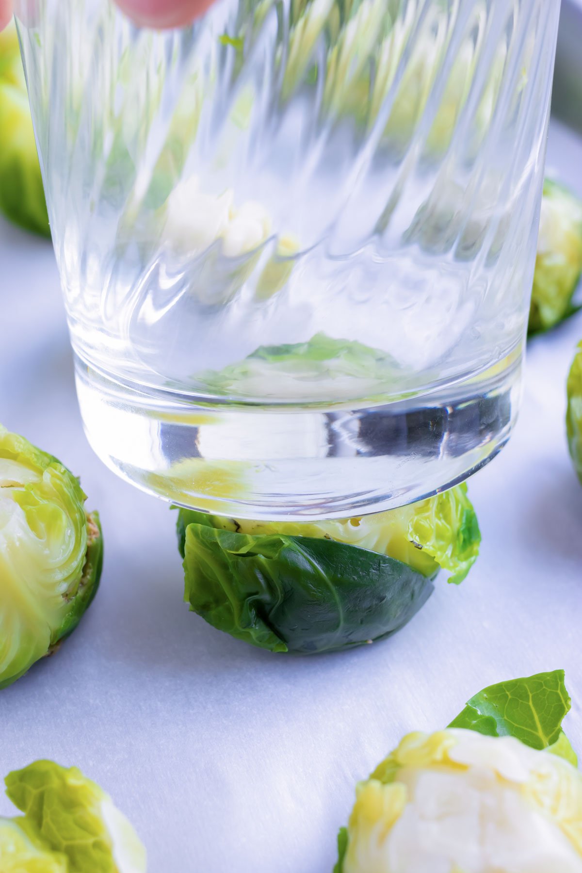 The bottom of a glass is used to smash the boiled Brussels sprouts.