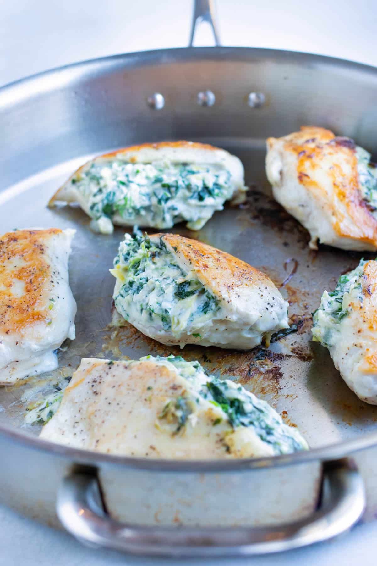 Spinach artichoke stuffed chicken is made in a skillet on the stove.