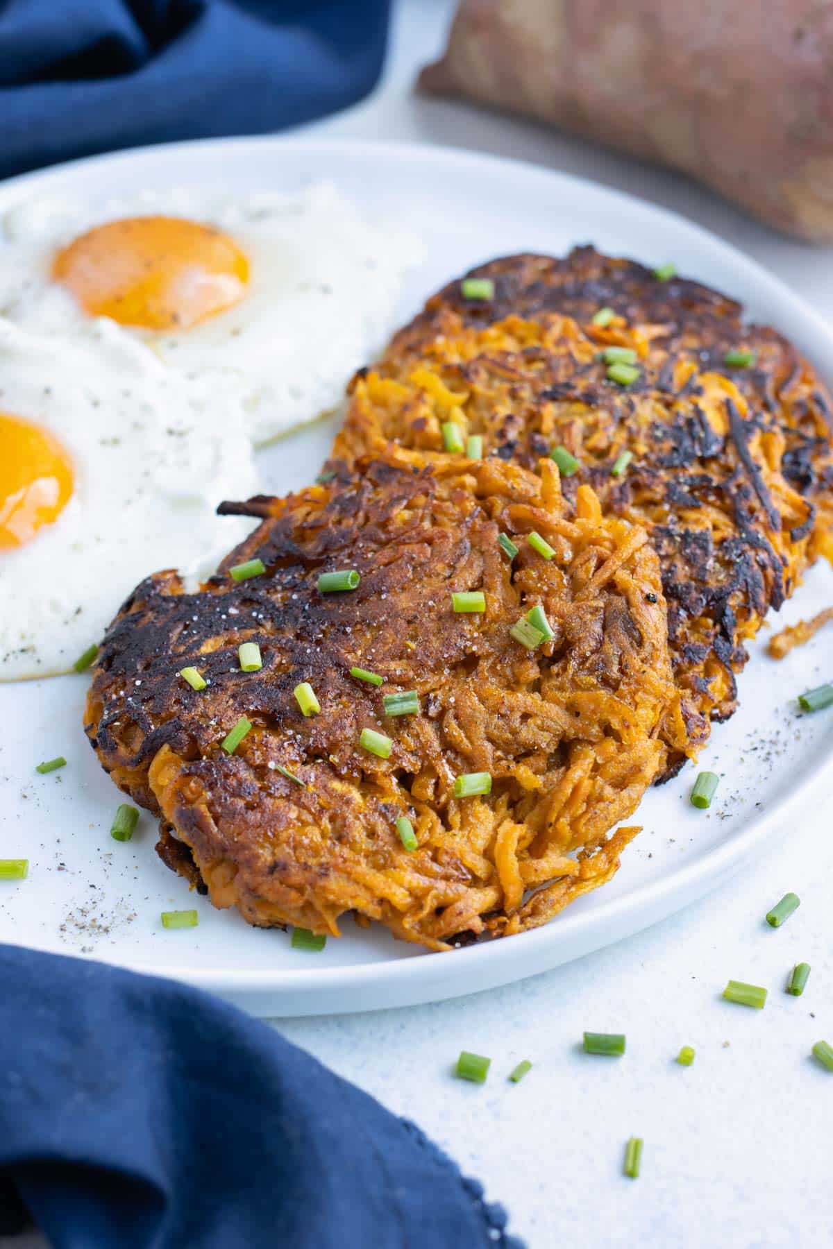 Crispy hash browns are served with fried eggs on a plate.