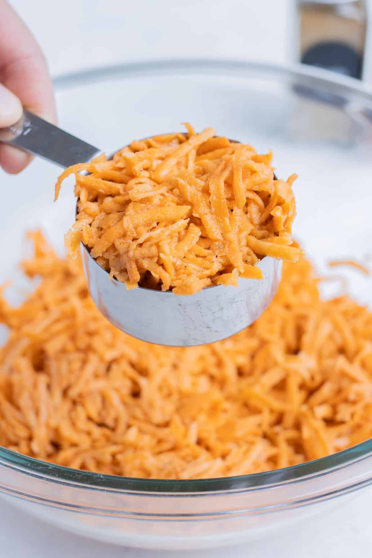 A measuring cup portions the mixture into evenly sized sweet potato hash brown patties.
