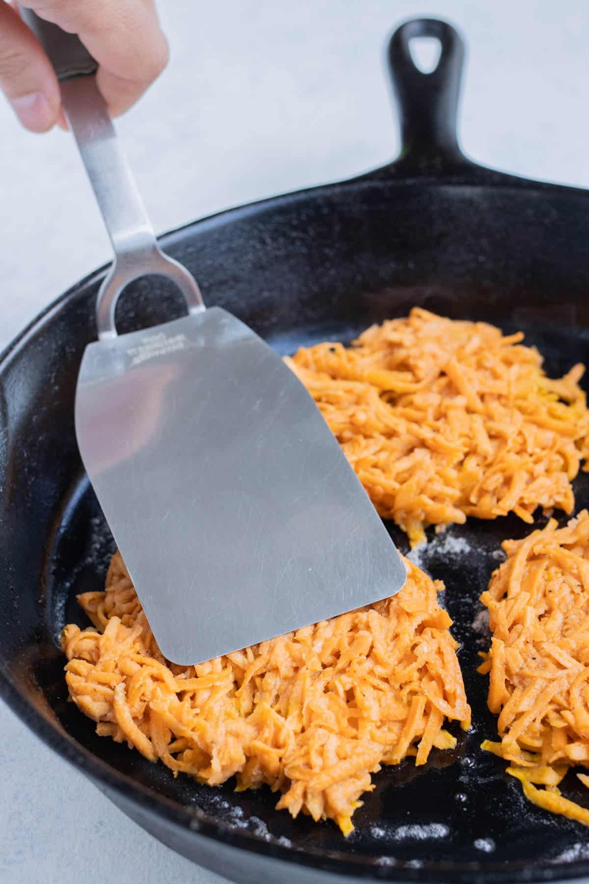 Sweet potato hash browns frying in butter in a cast iron skillet.