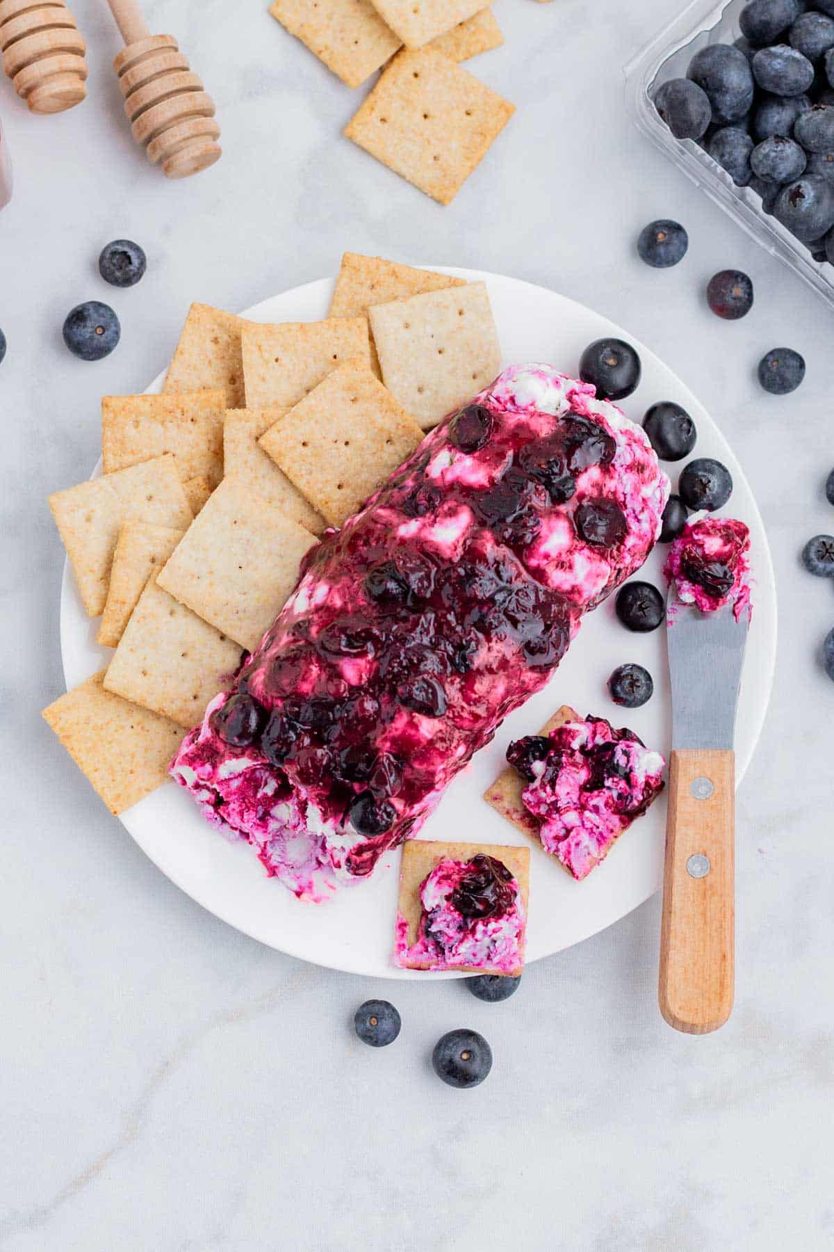 Blueberry goat cheese is spread on crackers with a cheese knife.