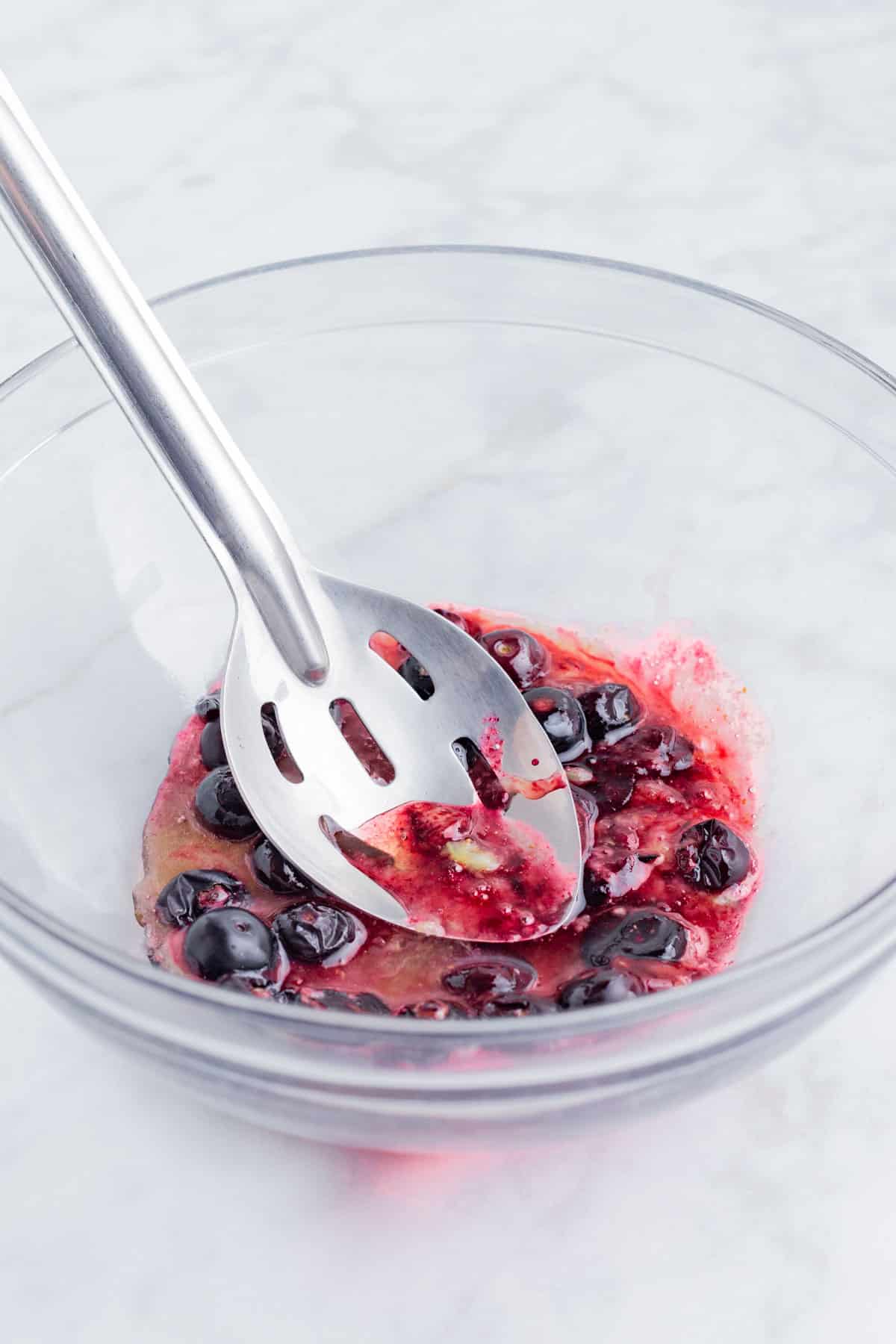 A slotted spoon mashes the heated bluberries.