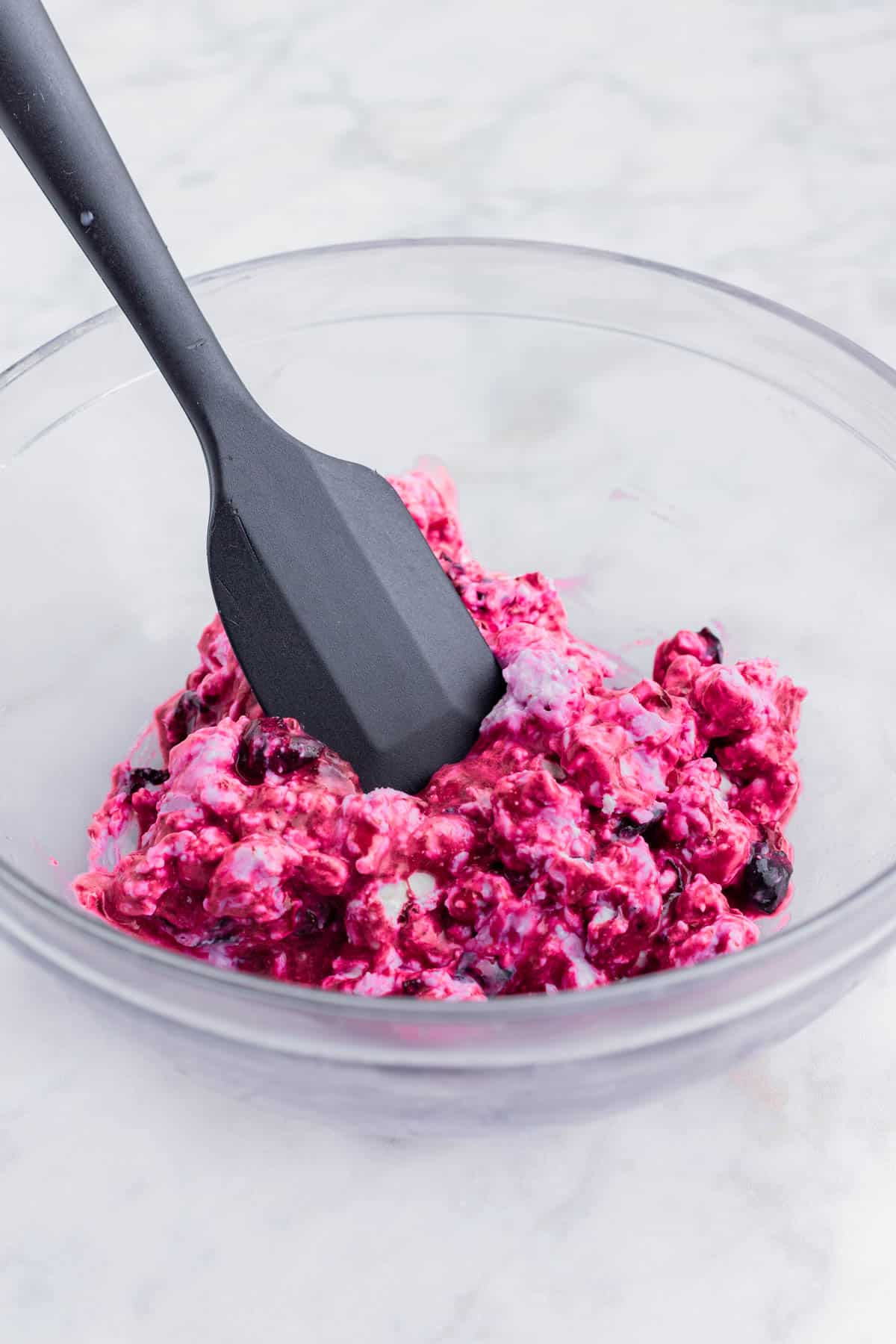 A spatula stirs goat cheese into the blueberry mixture