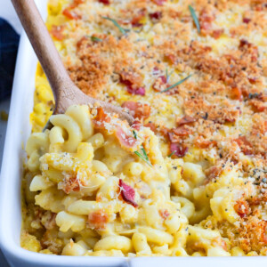 A wooden spoon digs into a pan of mac and cheese with butternut squash.